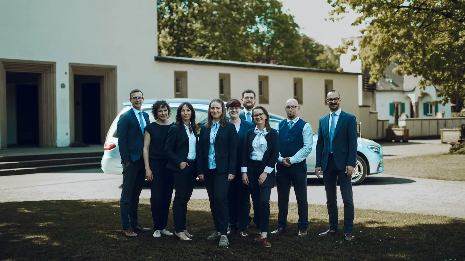 Das Team der Trauerhilfe Göck vor der Trauerhalle mit dem Bestattungswagen